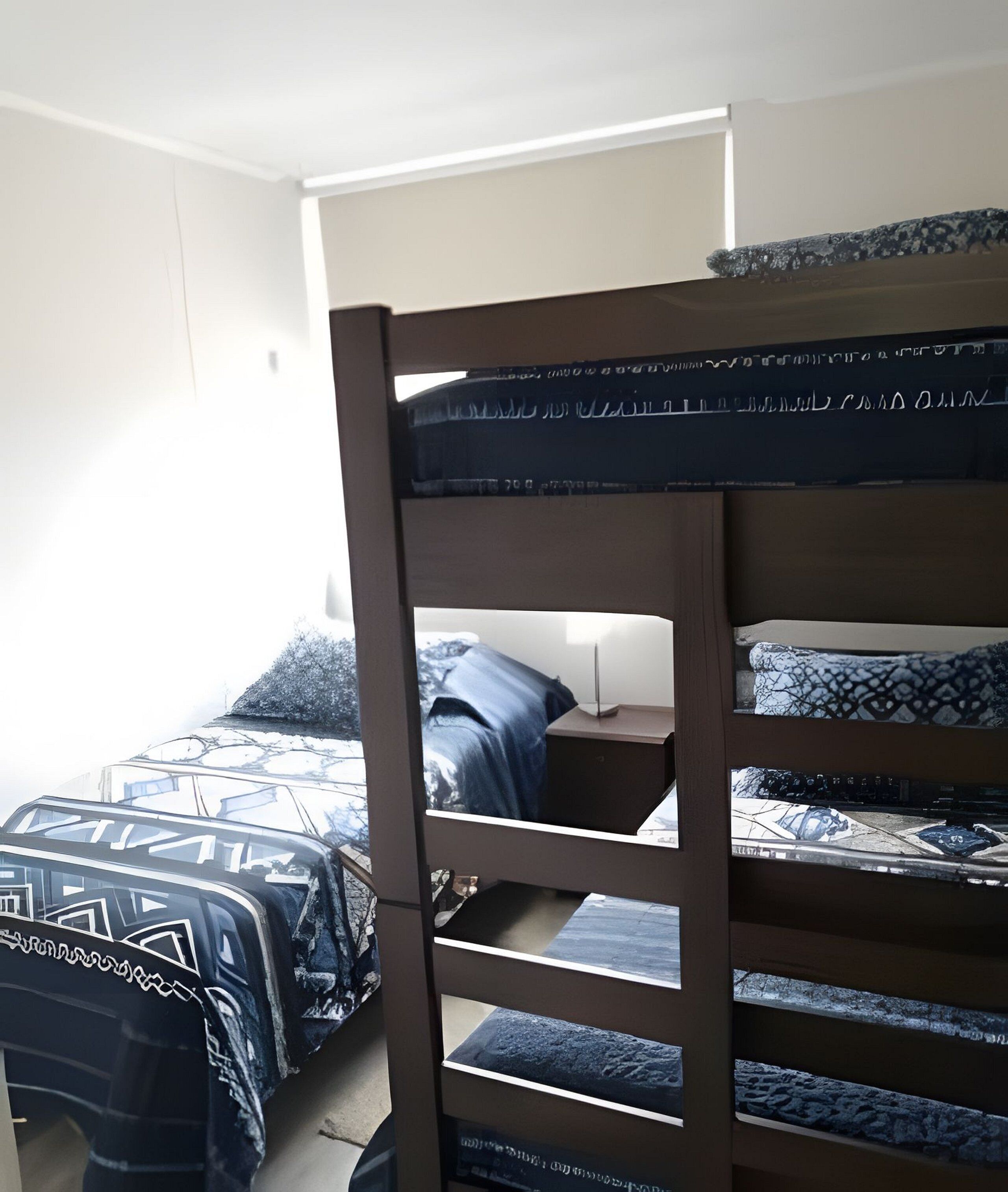 A bunk bed with patterned bedding, a bedside table, and a window with a view of the outside.