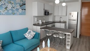 Une cuisine moderne avec des meubles blancs, un réfrigérateur en acier inoxydable et un coin repas doté d’un tabouret de bar.