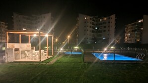 Ett utomhusområde som är öppet på kvällen och som har en pool, en möblerad sittplats under tak och angränsande bostadshus.