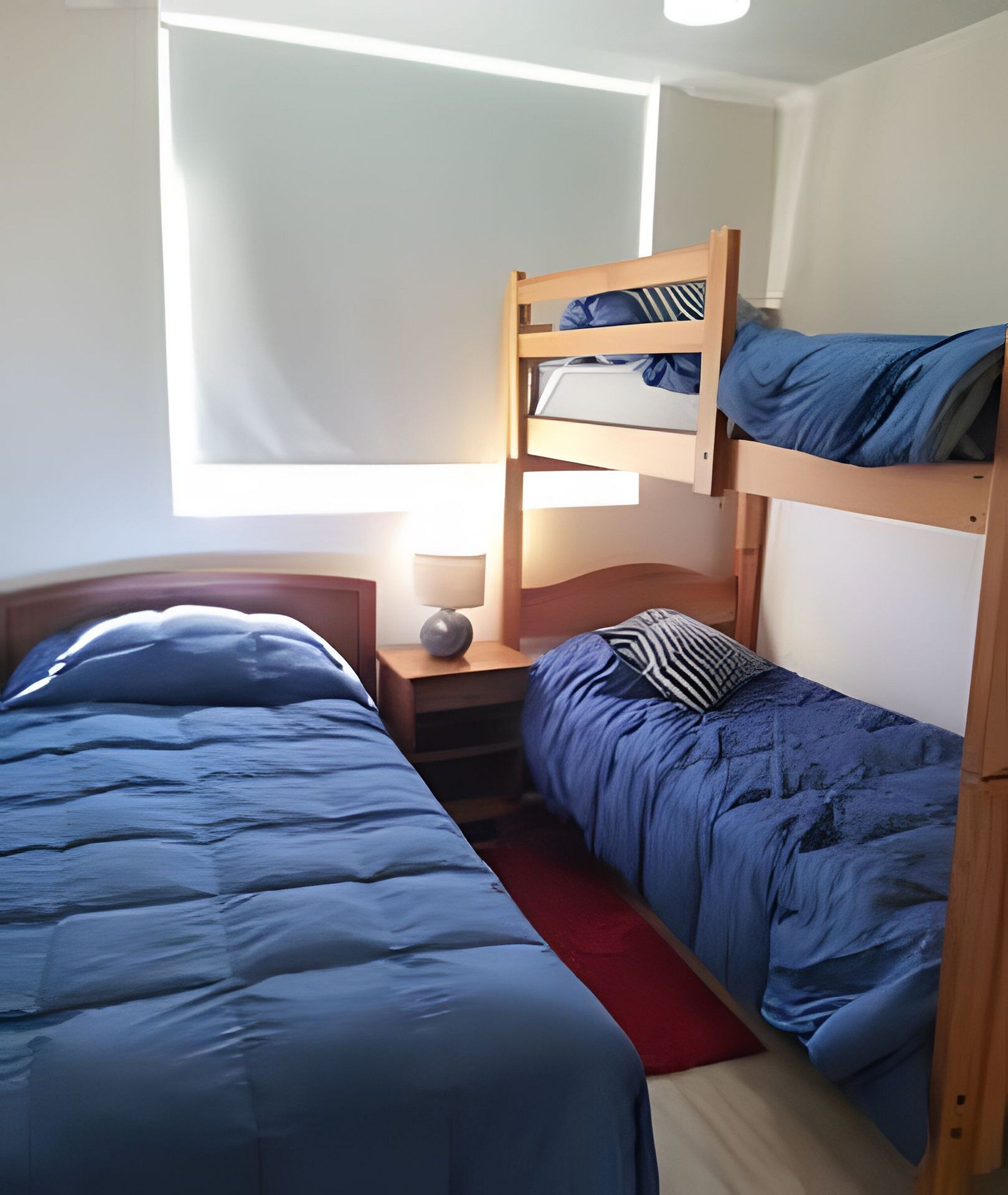 A bunk bed room with a desk and lamp, a window, and a red rug.