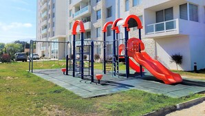 A playground with a slide and climbing structures, located in front of a multi-story residential building. - Dept. 5th Floor, Pacífico 2800 (La Serena)