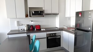 Une cuisine moderne avec des armoires blanches, des appareils en acier inoxydable et une chaise de couleur turquoise.