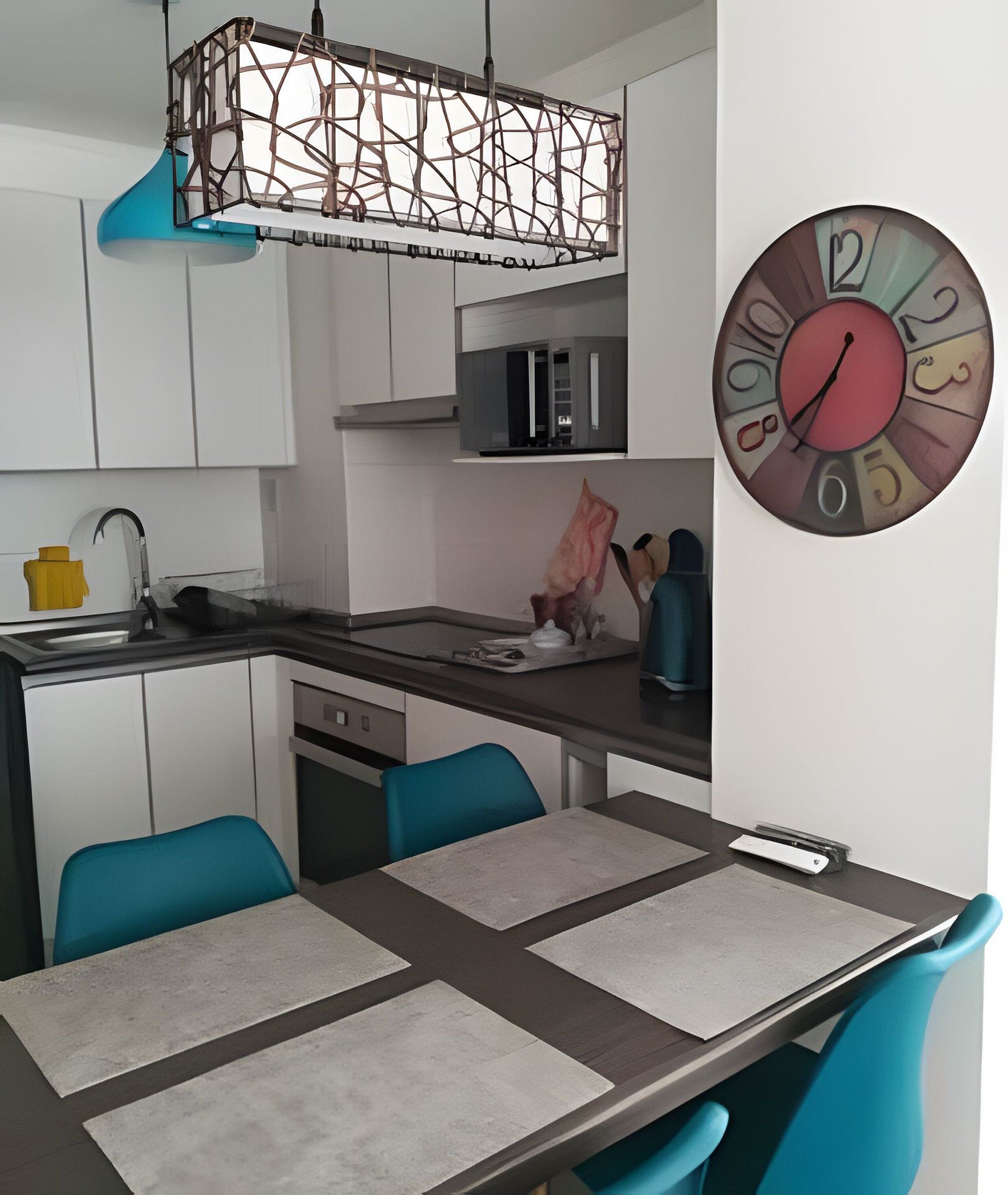 A modern kitchen with a dining area, a unique hanging light fixture, and a decorative clock on the wall.