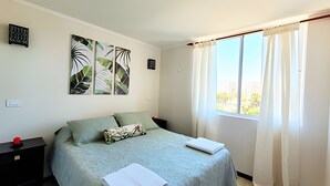 A bedroom with a bed, a nightstand, a window with curtains, and two wall art pieces. - 5th-floor apartment in a condo. Pacific 2800 (La Serena)