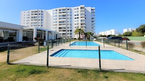 A modern building with a swimming pool, surrounded by a fence, and adjacent to a parking area. - 5th-floor apartment in a condo. Pacific 2800 (La Serena)