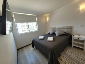 A bedroom with a bed, bedside tables, a window, and a view of buildings outside. - Apartment on the 3rd floor, ground level, at Pacífico 3100 (La Serena)