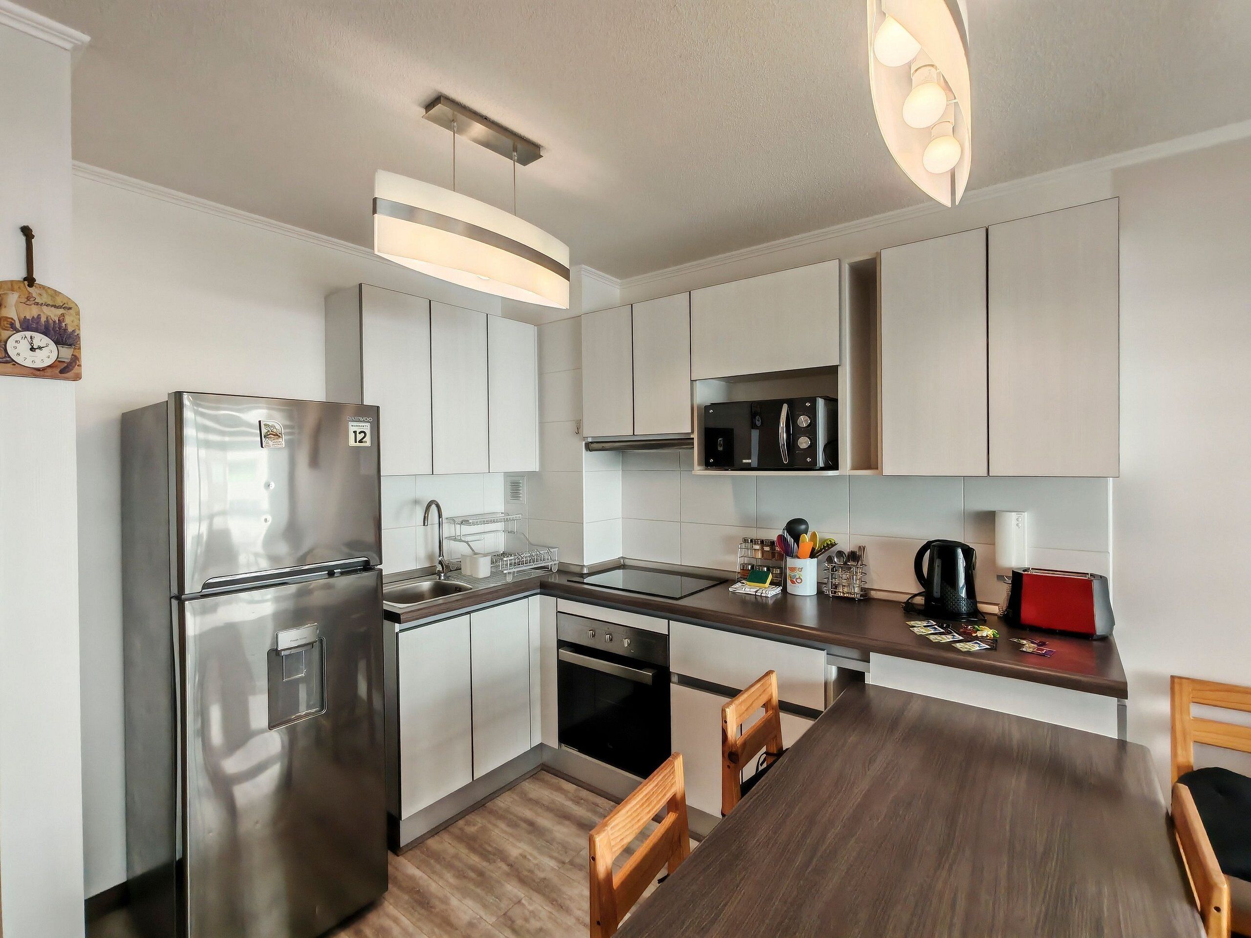 A modern kitchen with stainless steel appliances, a wooden dining table, and a pendant light.