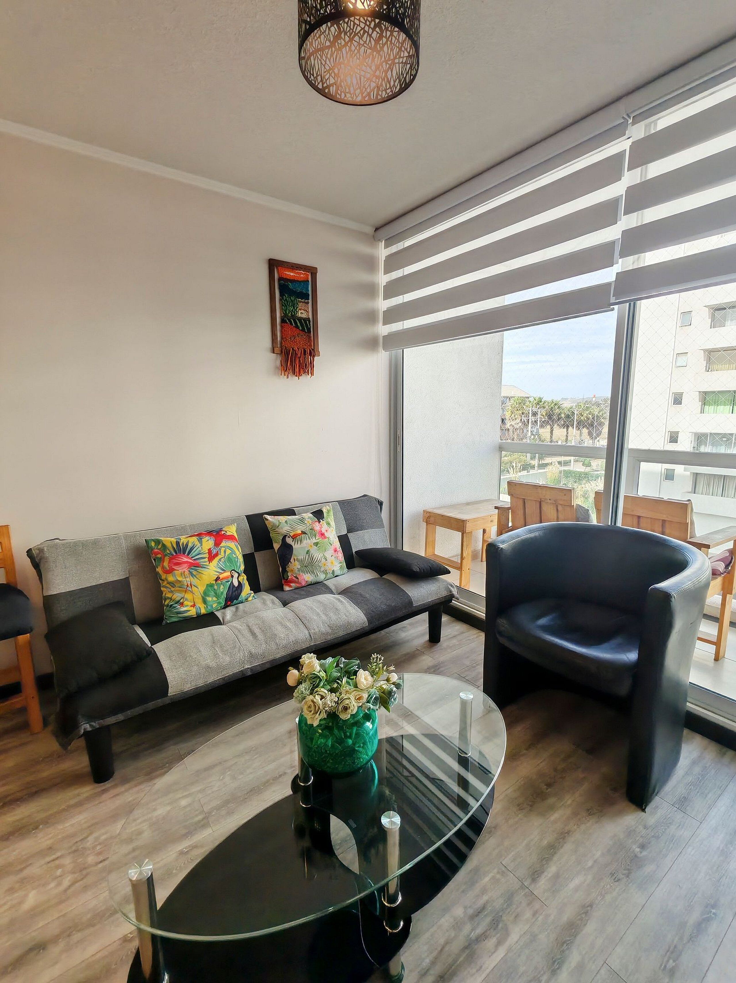 Un salon moderne avec un canapé, une table basse en verre et une vue sur un immeuble à travers de grandes fenêtres.