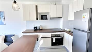 Una cocina moderna con armarios blancos, encimera de madera, microondas integrado y refrigerador.