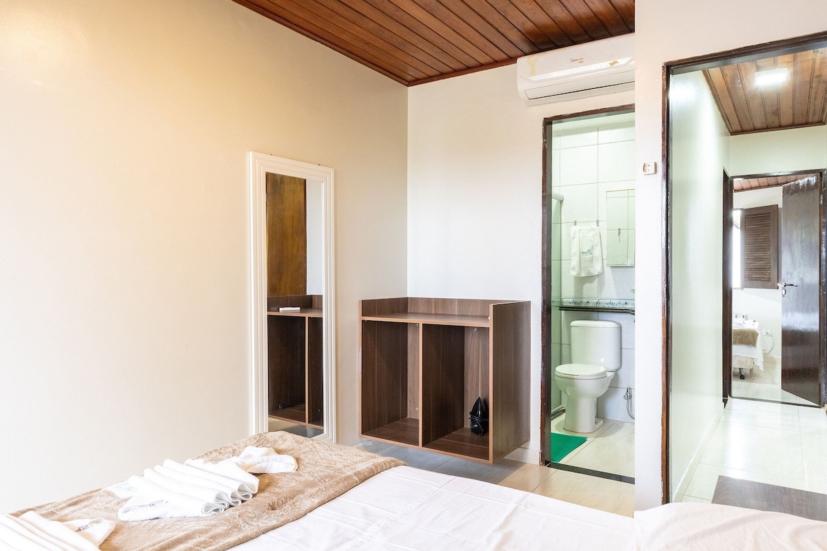 Ein Hotelzimmer mit einem Bett, einem Holzschrank, einem Badezimmer mit Toilette und Dusche sowie einer Glastür, die in einen anderen Raum führt.
