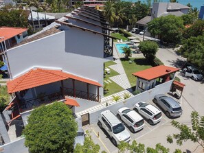 Ein mehrgeschossiges Gebäude mit einem rotgedachten Bauwerk, einem Schwimmbecken und einem Parkplatz mit mehreren Autos.