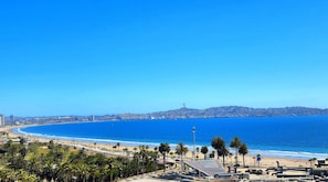 Eine Küstenstadt mit Strand, Palmen und einem markanten Hügel mit einem Turm in der Ferne.