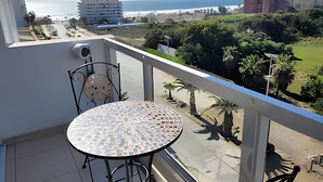 A balcony with a round table and chairs, overlooking a coastal area with buildings and greenery. - Apartment, 8th floor, Pacífico 2800 (La Serena)