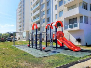 A playground with a slide and climbing structures, located in front of a multi-story residential building.