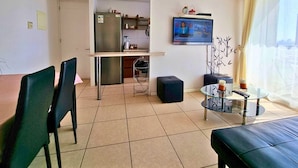Una sala de estar moderna con comedor, cocina y un televisor que muestra un noticiero.