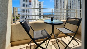Un balcón con dos sillas y una mesa, con vistas a un paisaje urbano de edificios altos.