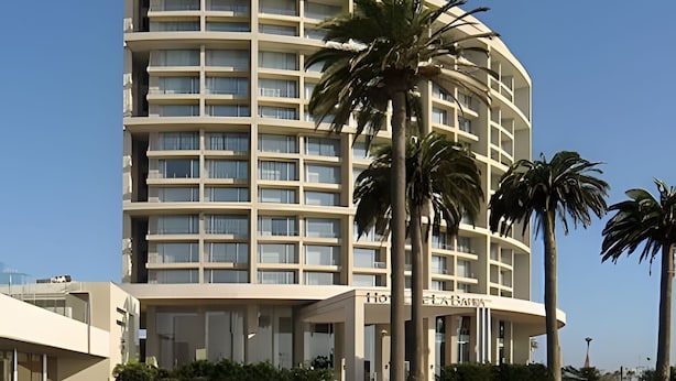 Un hotel de varios pisos con fachada curva, balcones y palmeras en primer plano.