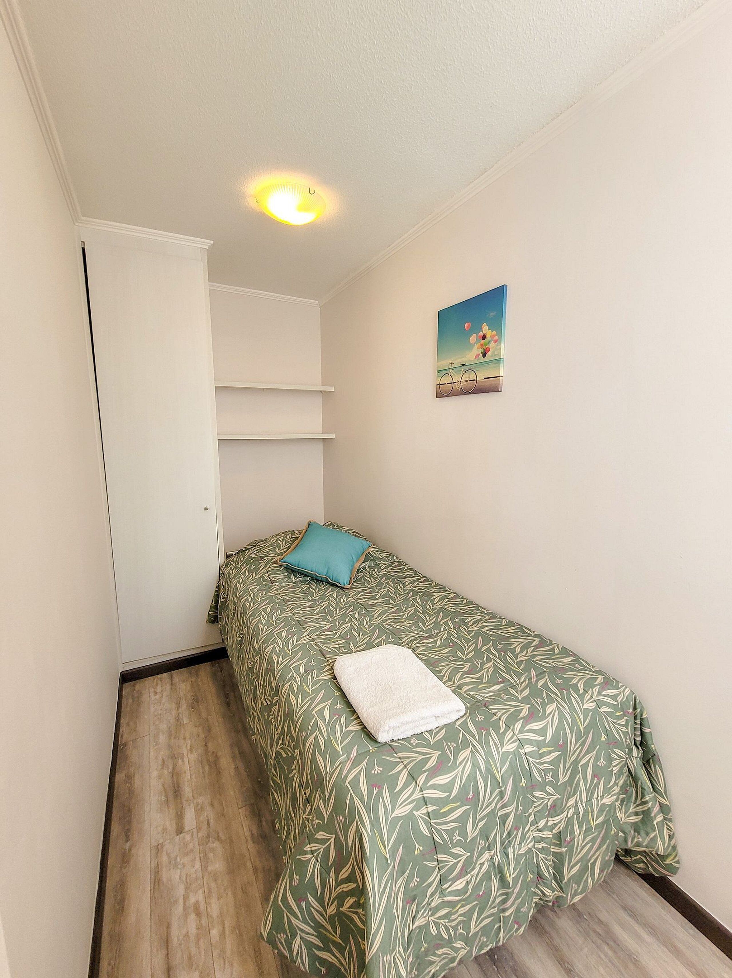 A small bedroom with a single bed, a white door, a shelf unit, and a painting on the wall.