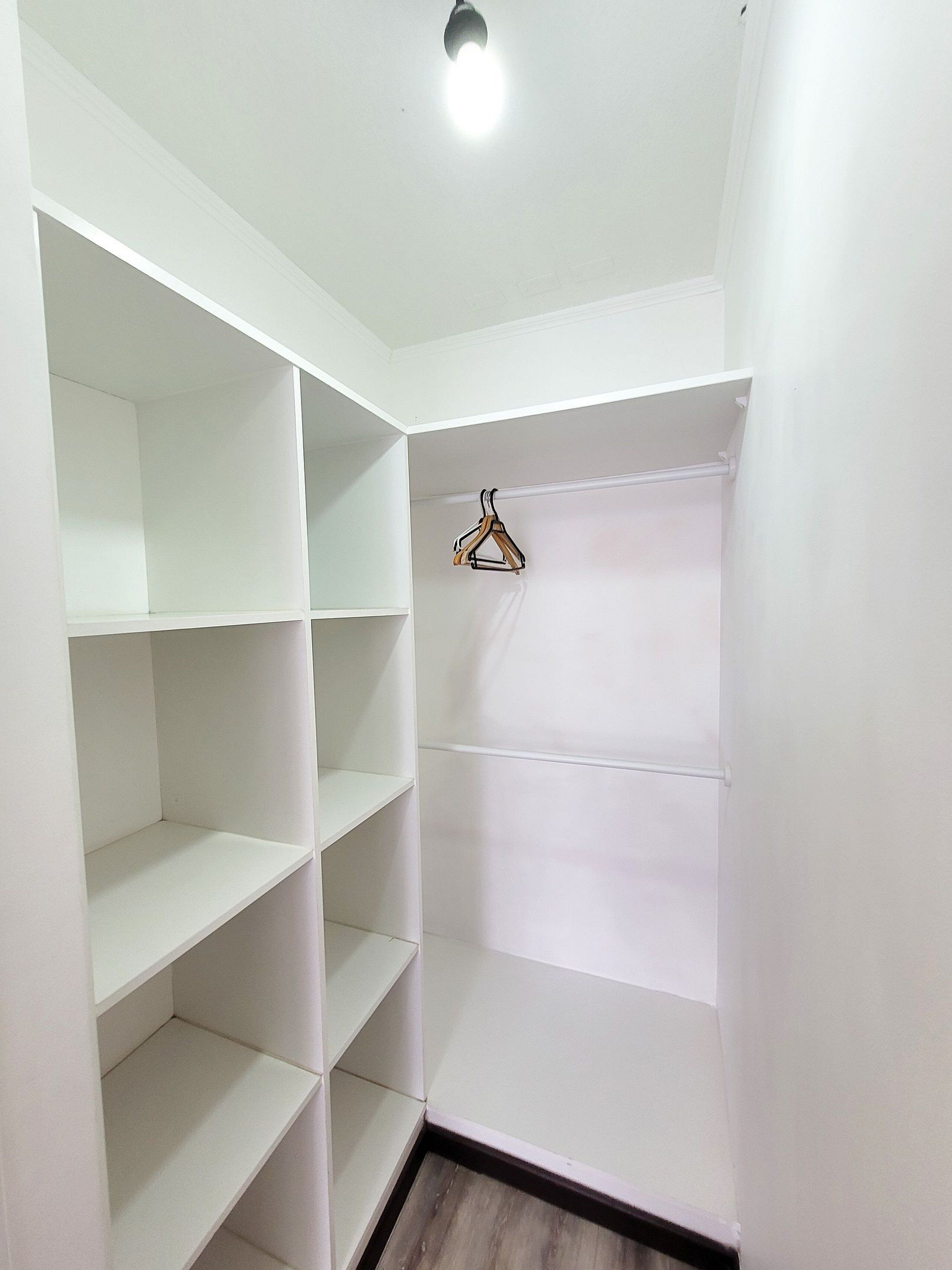 A corner closet with white shelves and a wooden hanger.