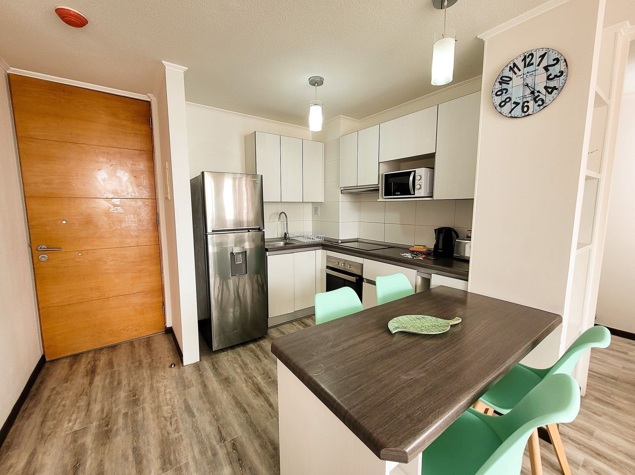 A compact kitchen with a refrigerator, microwave, sink, and a clock on the wall.