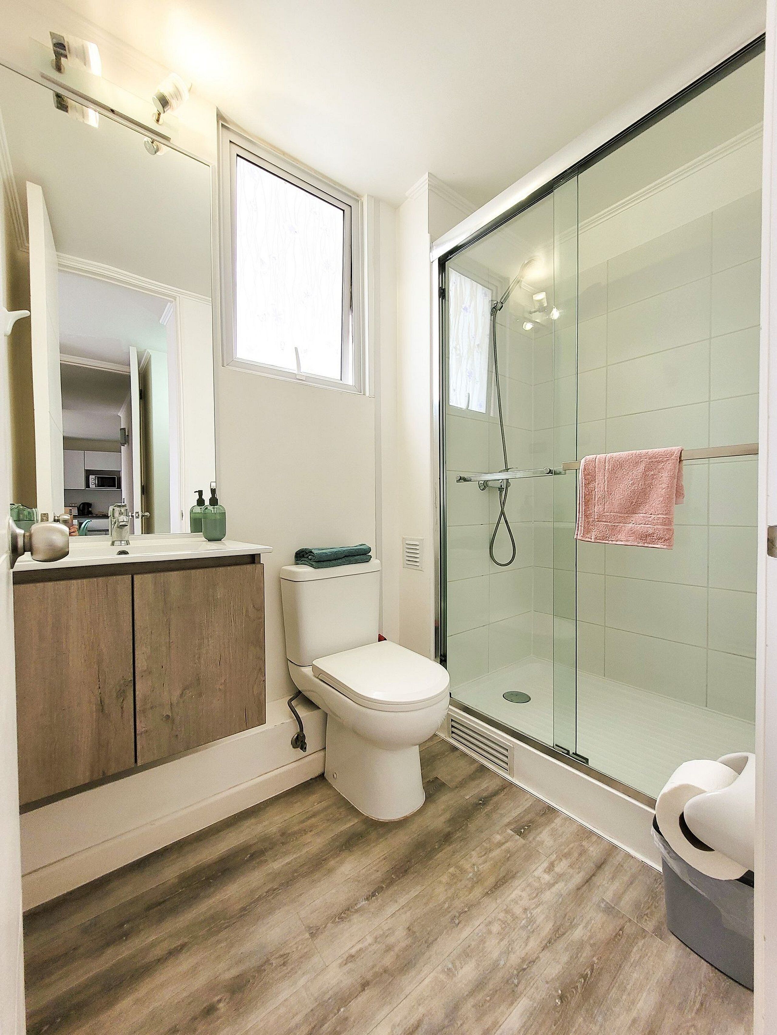 A modern bathroom with a glass shower enclosure, a white toilet, and a wooden vanity.