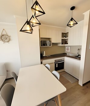 A modern kitchen with white cabinets, a microwave, and a sink. There is a dining table with chairs. - Dept. 5th Floor, Distrito Verde (La Serena)