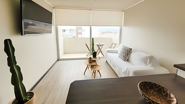 A modern living room with a sofa, a dining table, a cactus, and a TV mounted on the wall. - Dept. 10th Floor, Cond. Pacific II (La Serena)