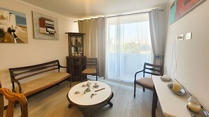 A room with a sofa, a dining table, a small round table with items, a cabinet, and a view through a window. - Dept. 3rd Floor, Pacífico 2800 (La Serena)