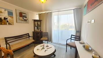 A room with a sofa, a dining table, a small round table with items, a cabinet, and a view through a window.