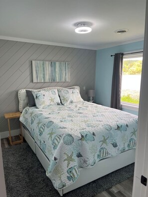 A bedroom with a bed, a nightstand, a lamp, a window with curtains, and a ceiling light.