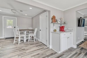 A modern kitchen with white cabinetry, a wooden dining table, and a red coffee maker.