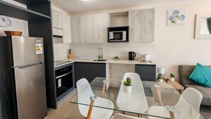 Una cucina moderna con frigorifero, microonde e piano cottura. È presente un'area pranzo con un tavolo in vetro e sedie.
