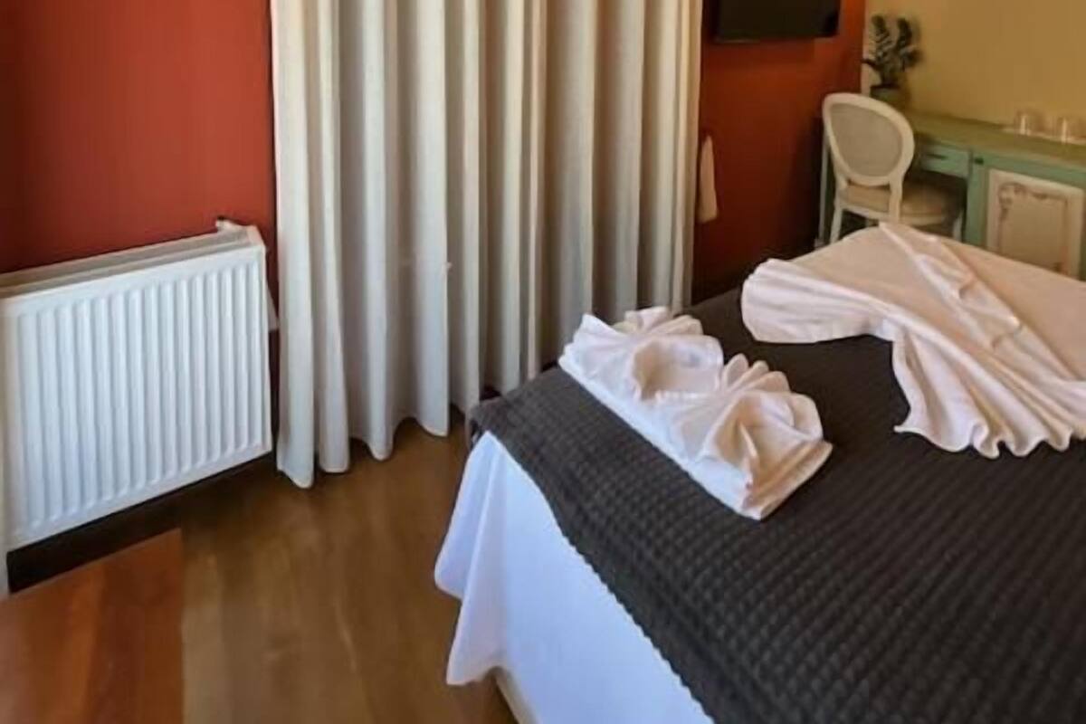 Une chambre d’hôtel avec un lit, une fenêtre avec des rideaux, un radiateur et une lampe fixée au mur.
