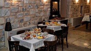 A stone-walled dining area with tables set for breakfast, including plates of food, cups, and a coffee machine.