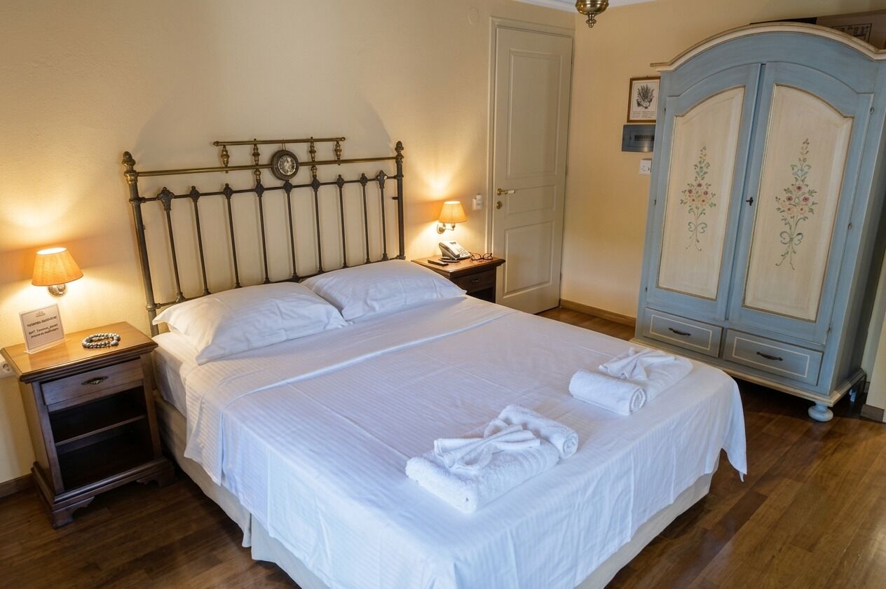 Un llit ben fet amb roba de llit i tovalloles blancs, una làmpada de nit, una petita taula de nit amb una làmpada, i un armari amb motius florals.