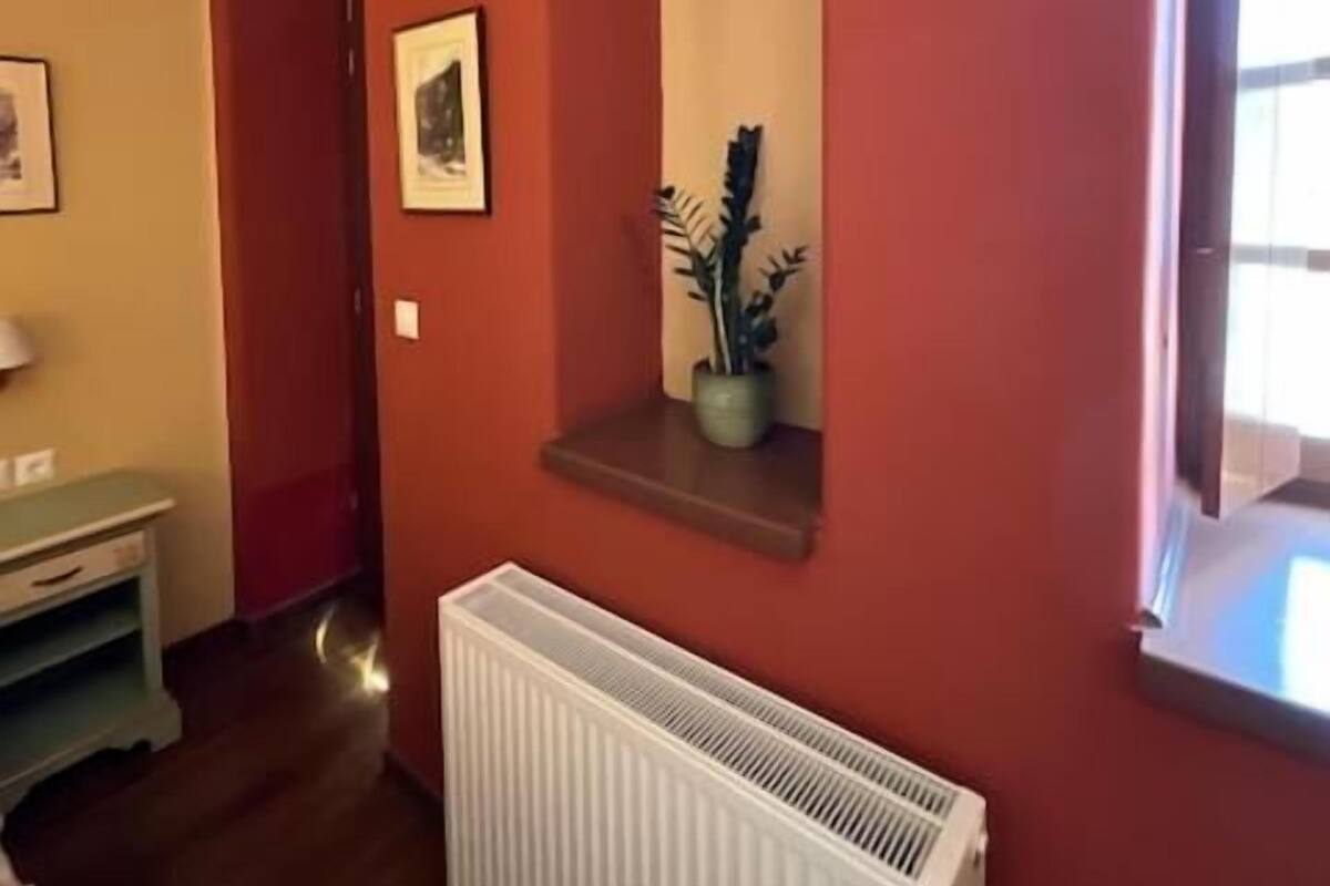 Une pièce avec un radiateur, une fenêtre avec un rideau et une petite étagère sur laquelle se trouve une plante.