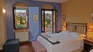A bedroom with a bed, two bedside tables, a bench, and two windows with a mountain view.