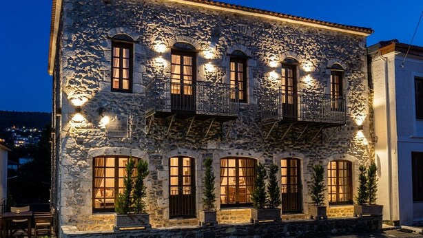 A stone building with multiple windows and balconies, featuring outdoor seating and potted plants.