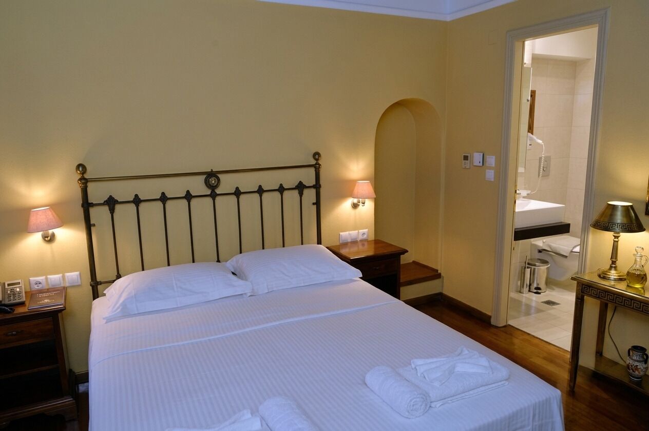 A hotel room with a bed, bedside lamps, a nightstand, a table with a lamp, and a bathroom visible through an archway.