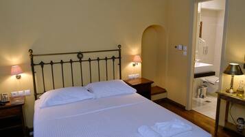 A hotel room with a bed, bedside lamps, a nightstand, a table with a lamp, and a bathroom visible through an archway.