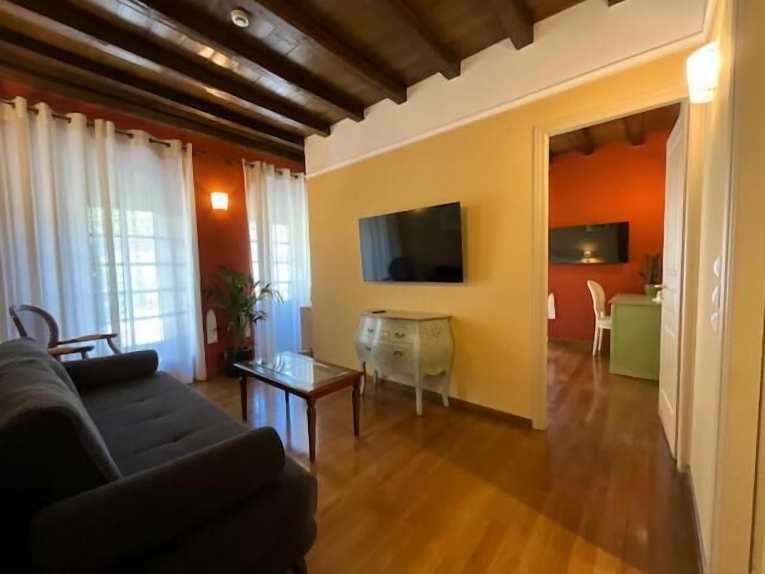 A living room with a sofa, a TV, a small table, and a kitchen area in the background.