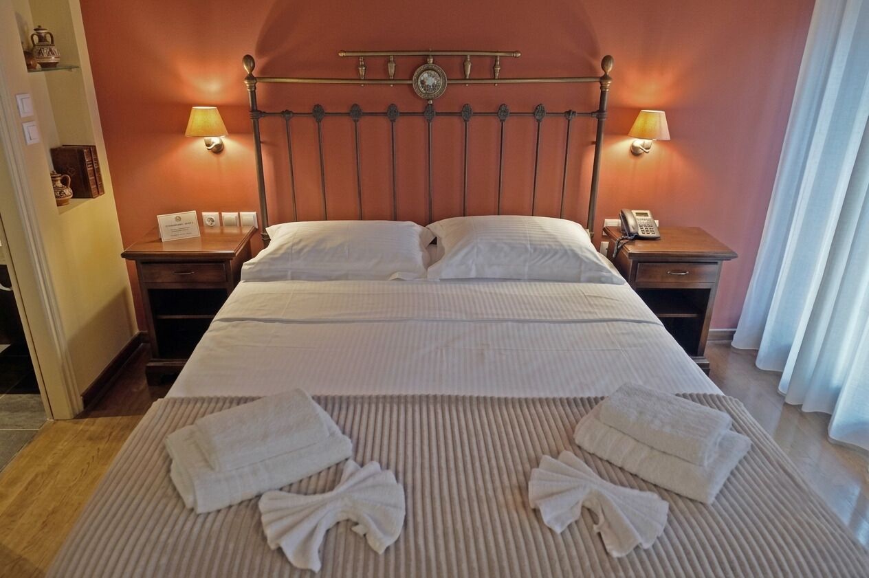 A hotel room with a bed, two bedside tables, a nightstand, and a lamp.