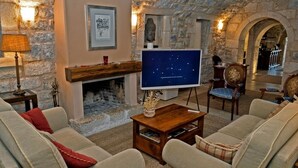 A cozy living room with stone walls, a fireplace, a television, and comfortable seating.