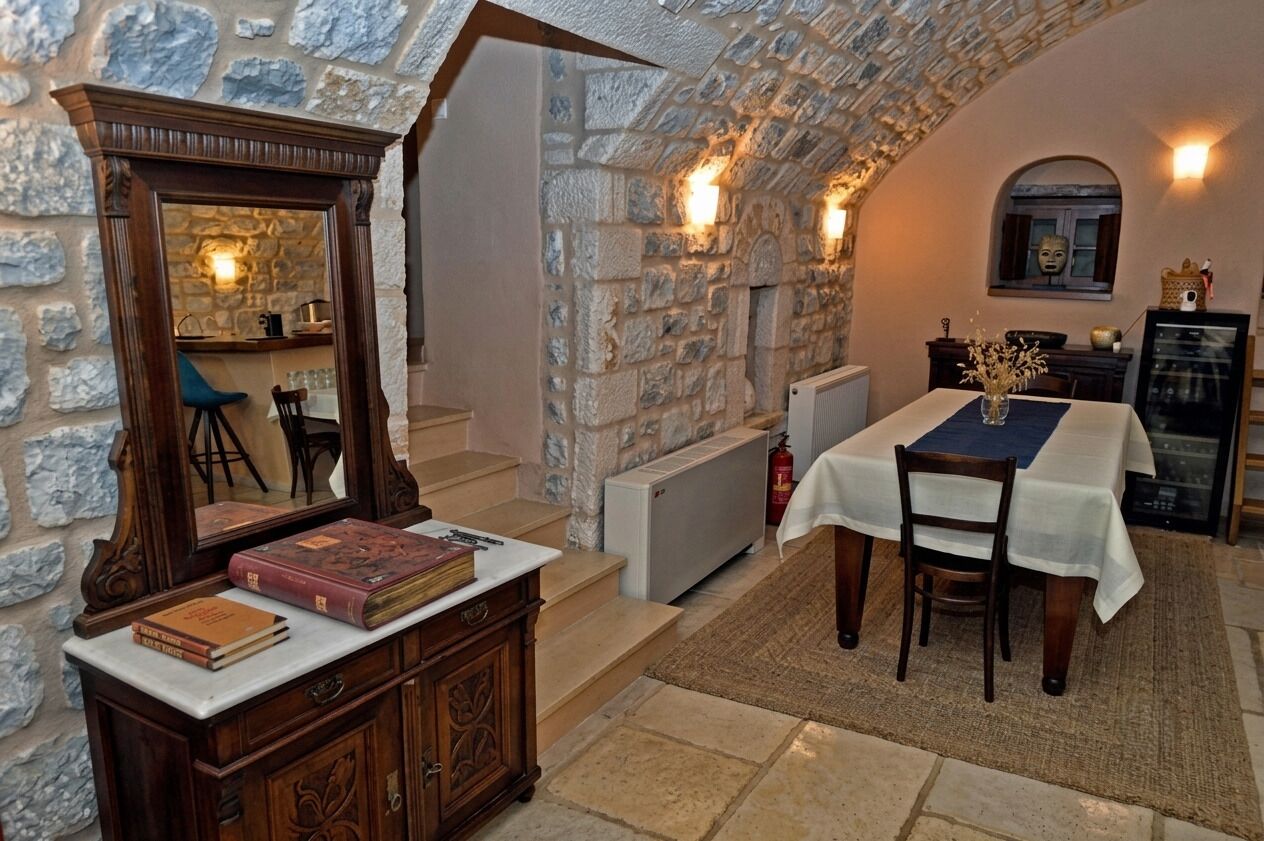 A stone-walled room with a dining table, chairs, a mirror, and a fireplace.