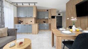 Eine moderne Küche mit grauen Schränken, einem Essbereich mit Holztisch und einem an der Wand montierten Flachbildfernseher.