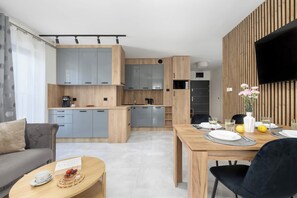 Eine moderne Küche mit grauen Schränken, einem Essbereich mit Holztisch und einem an der Wand montierten Flachbildfernseher.