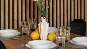 Ein Esstisch ist gedeckt mit Tellern, Gläsern und einer Blumenvase.