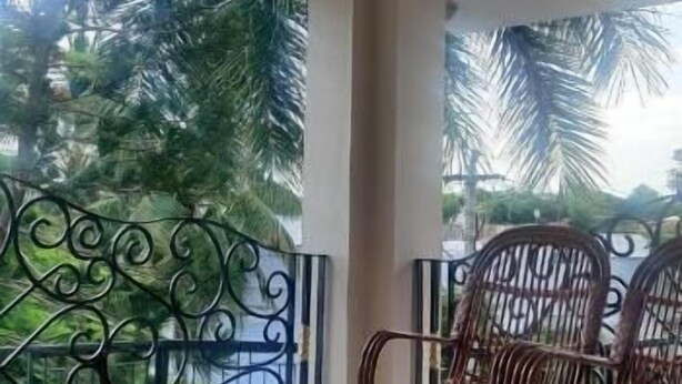 Una habitación con ventilador de techo, ventanas amplias con barandillas metálicas y mobiliario de mimbre.