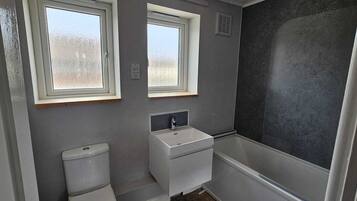 A small bathroom with two windows, a toilet, a sink, and a shower.