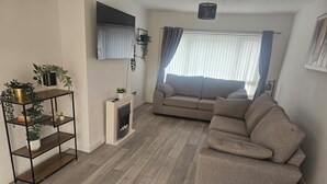Un salon avec un canapé, un téléviseur fixé au mur, une cheminée et un plancher en bois.